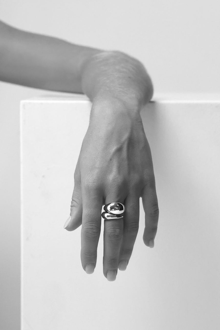 A black and white image of a hand wearing two chunky dome rings on the middle finger