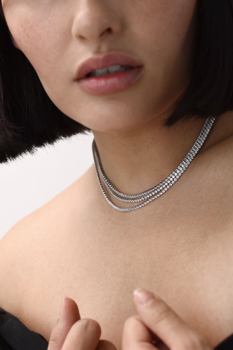 A close on of a woman's neck, as she has three tennis necklaces stacked