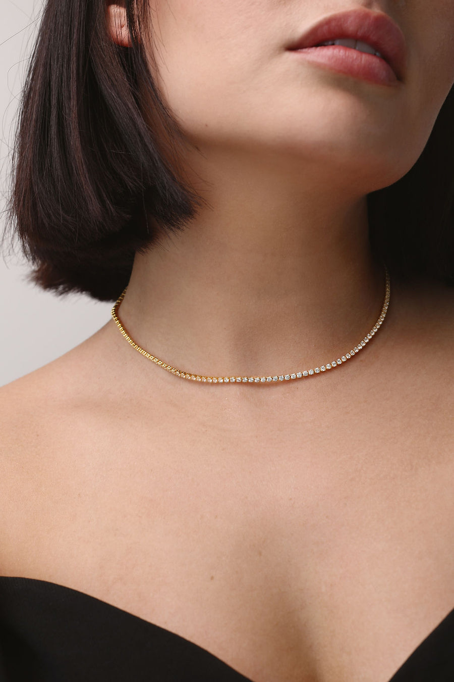 A close up of a woman's neck as she wear a gold tennis necklace
