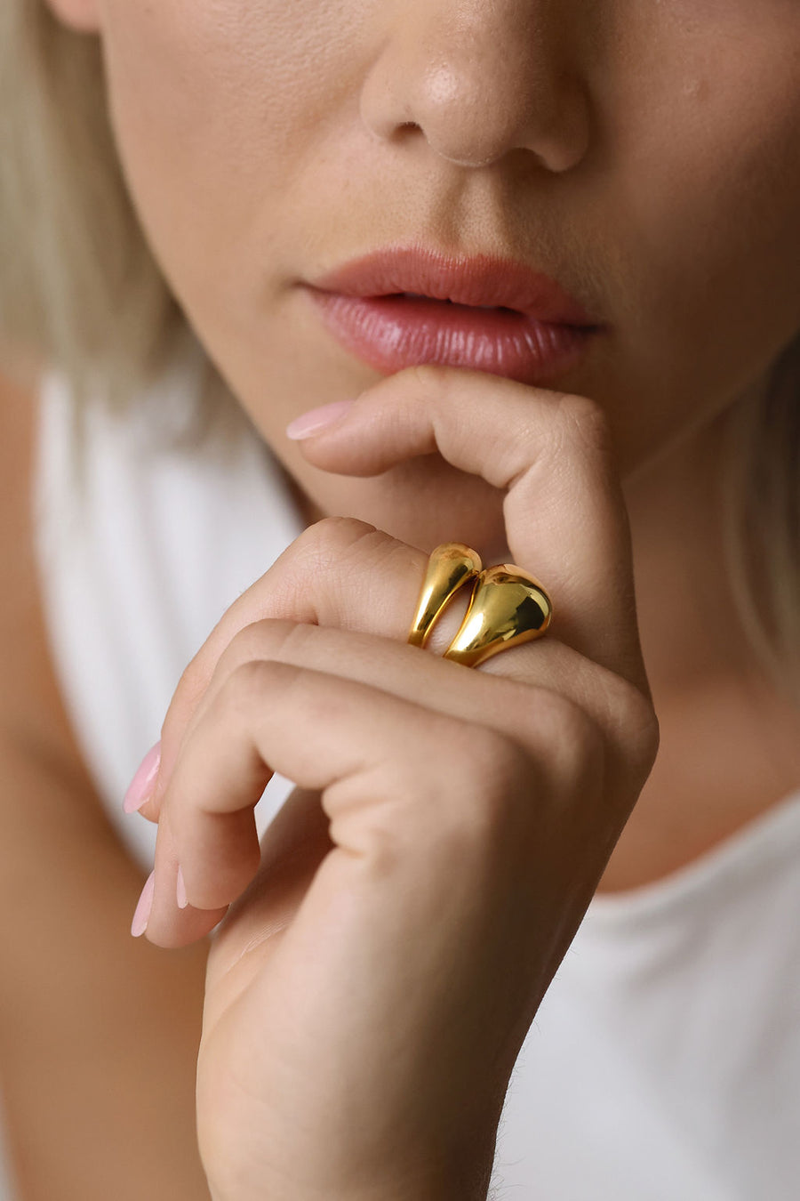 Close up on woman's hand against her chin, with focus on her two gold dome rings on her middle fingers
