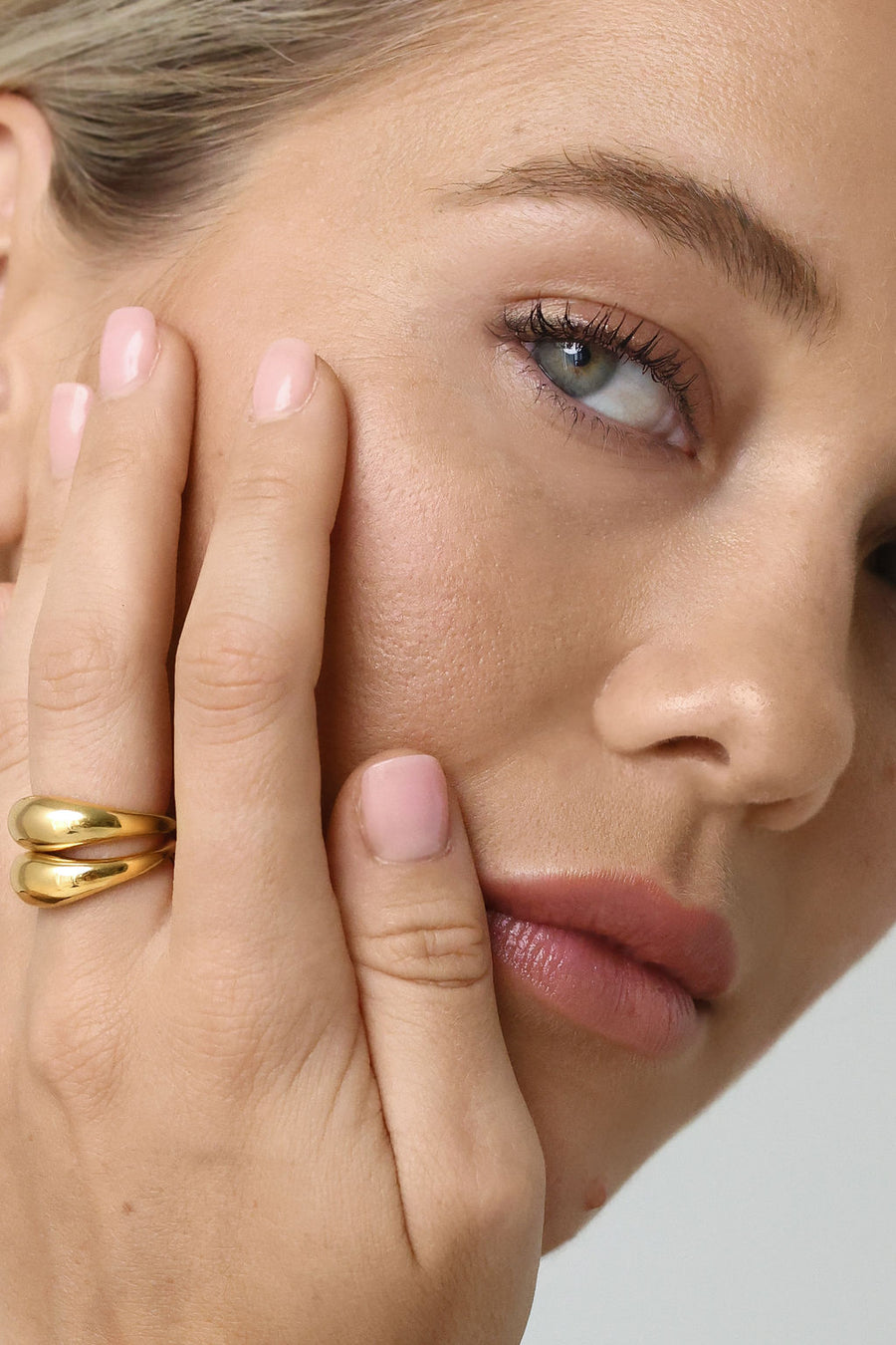 A close up on a woman's face, with her hand cupping her face as she wears her gold dome rings on her middle finger