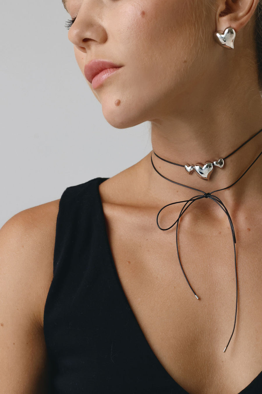 A close up of a woman's neck, showing the wrap necklace with silver heart pendants, and her chunky silver earrings