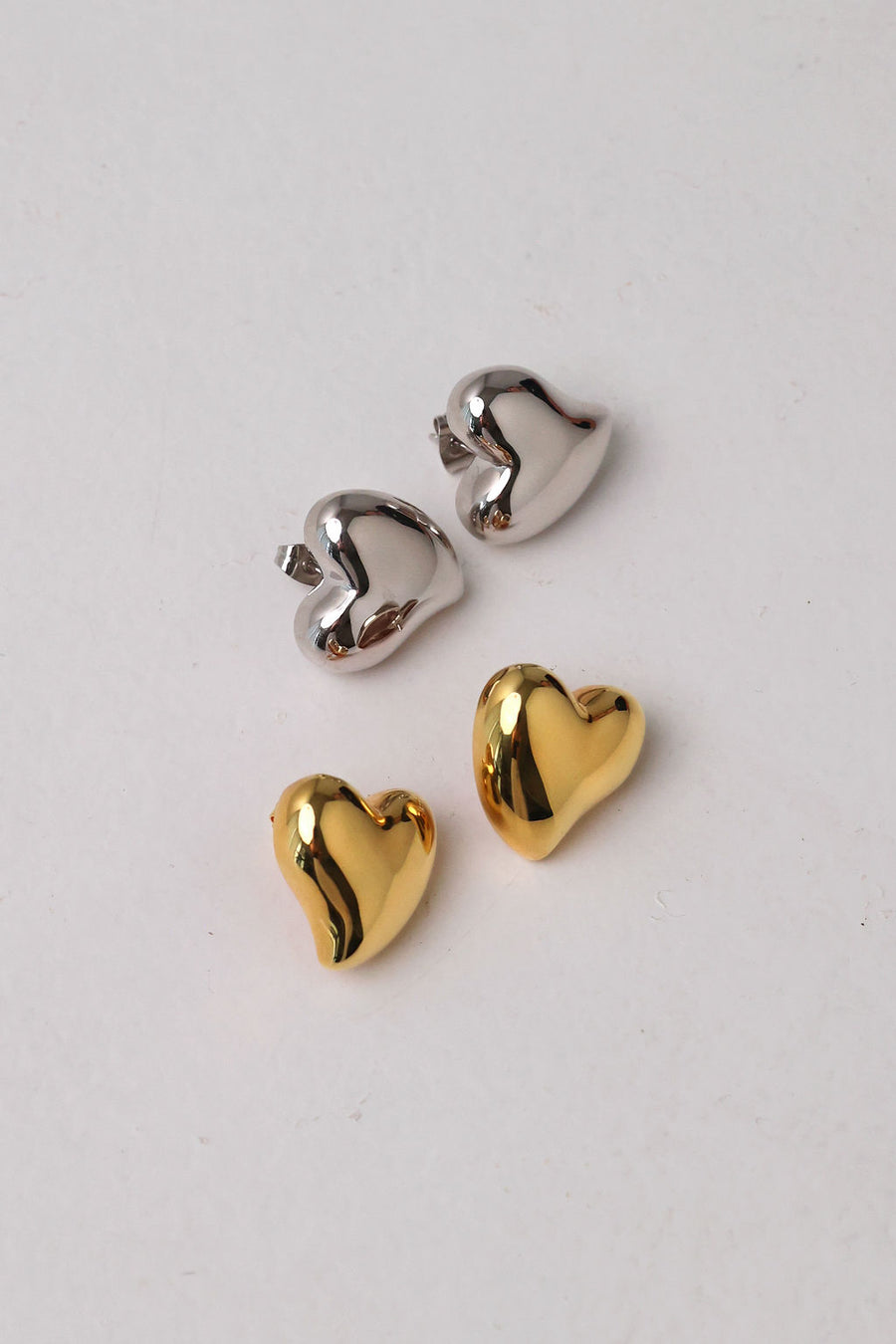 Flat lay image of oversized loveheart shaped studs in silver and gold