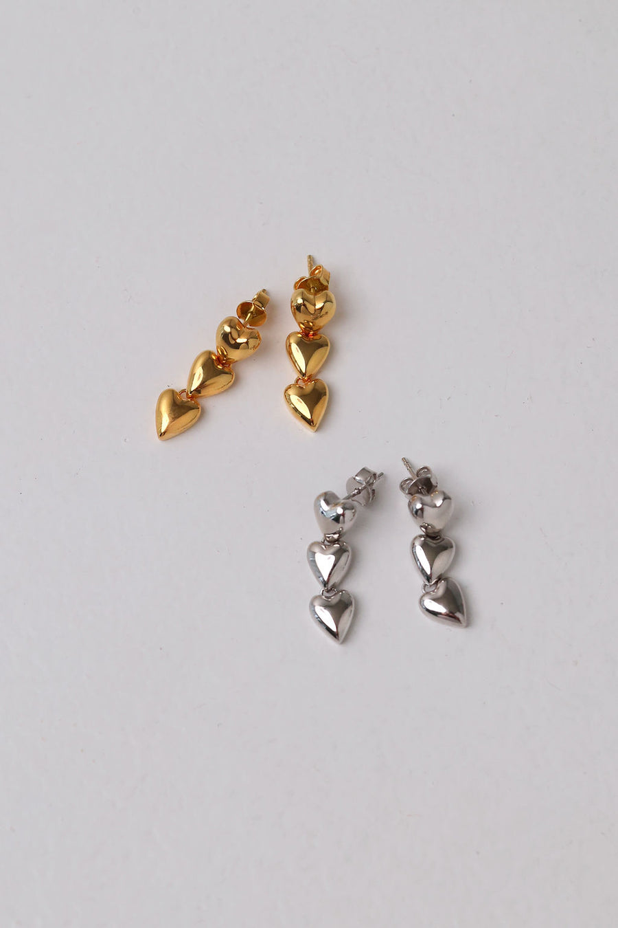 Flat lay image of gold and silver heart shaped drop earrings