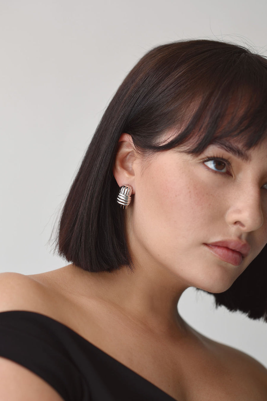Woman staring off into the distance, wearing a black off the shoulder top and chunky silver earrings