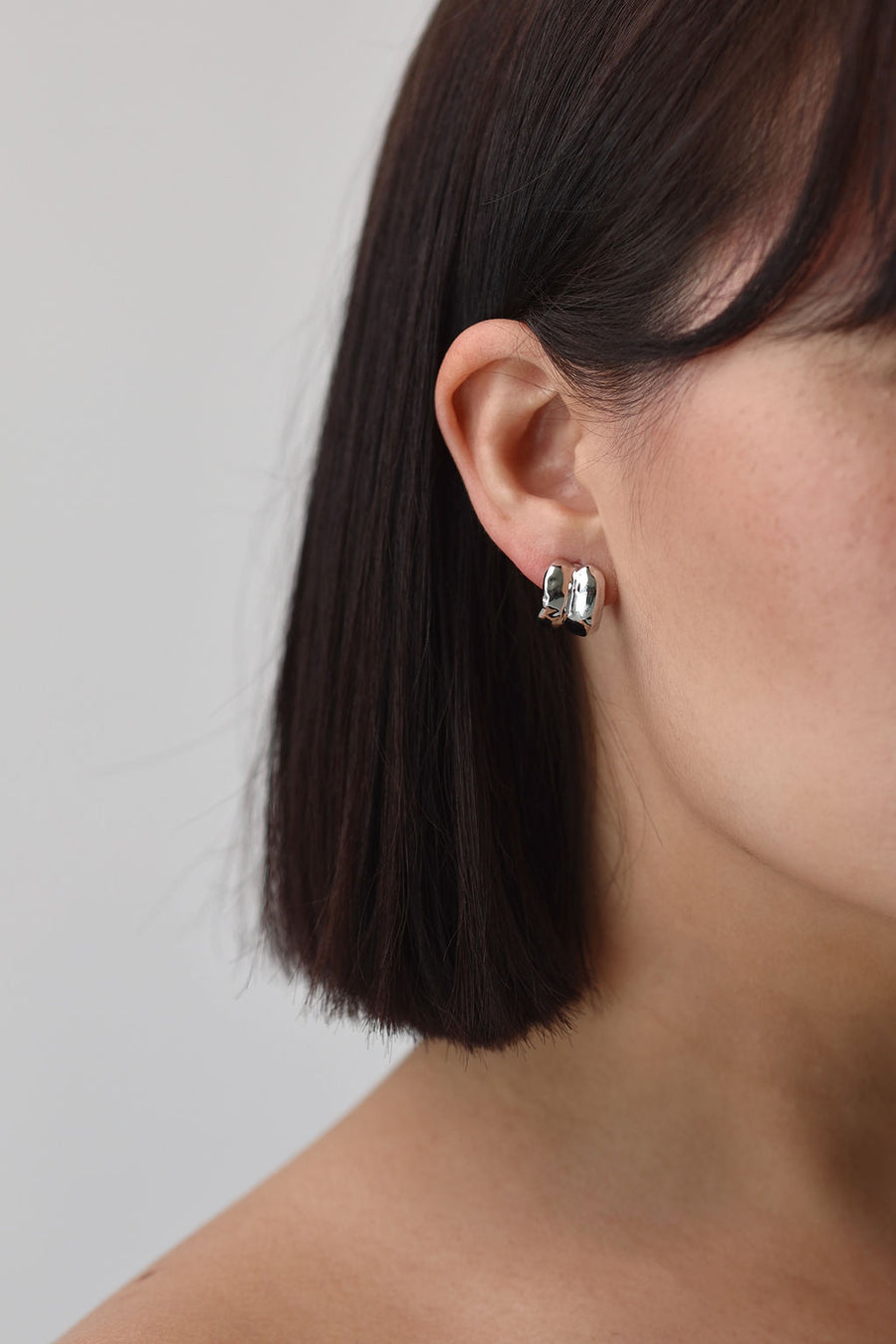 A close up of one side of a woman's face wearing a small chunky silver earring