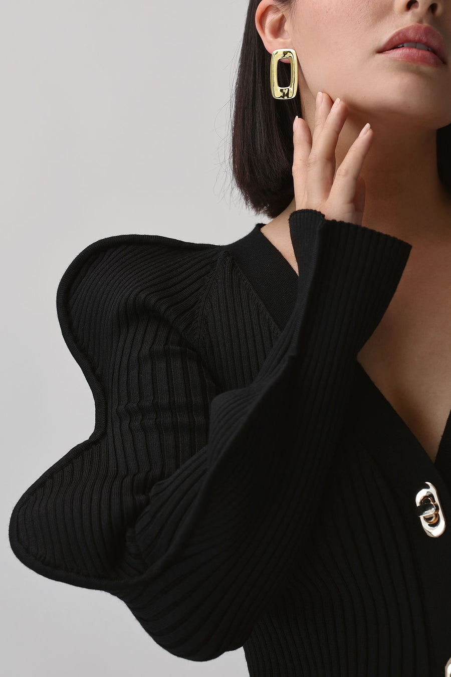 a close up shot of woman wearing a black knit and large gold earrings, touching the side of her jaw