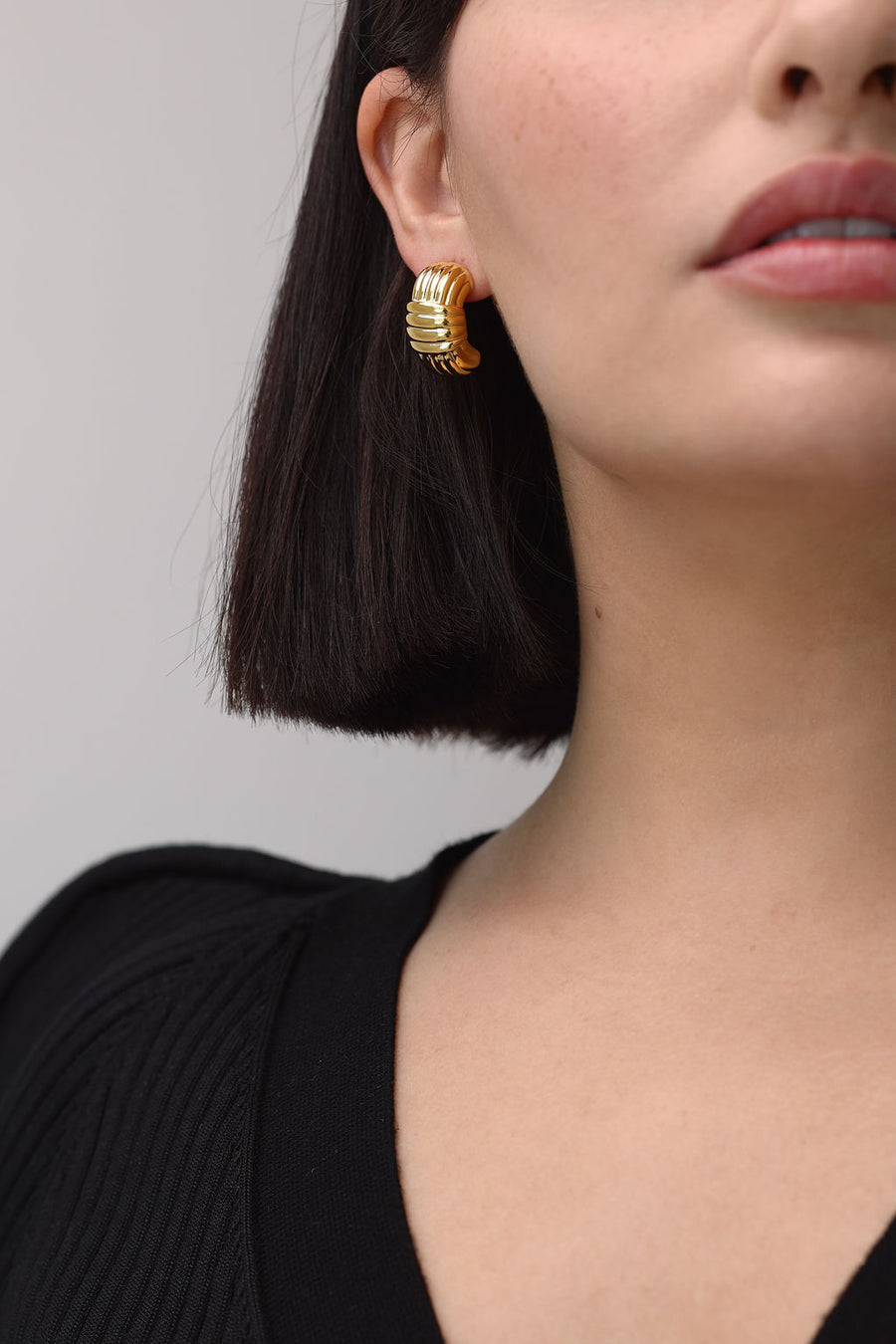 A close of up a chunky gold earring worn by a woman with bob length brown hair