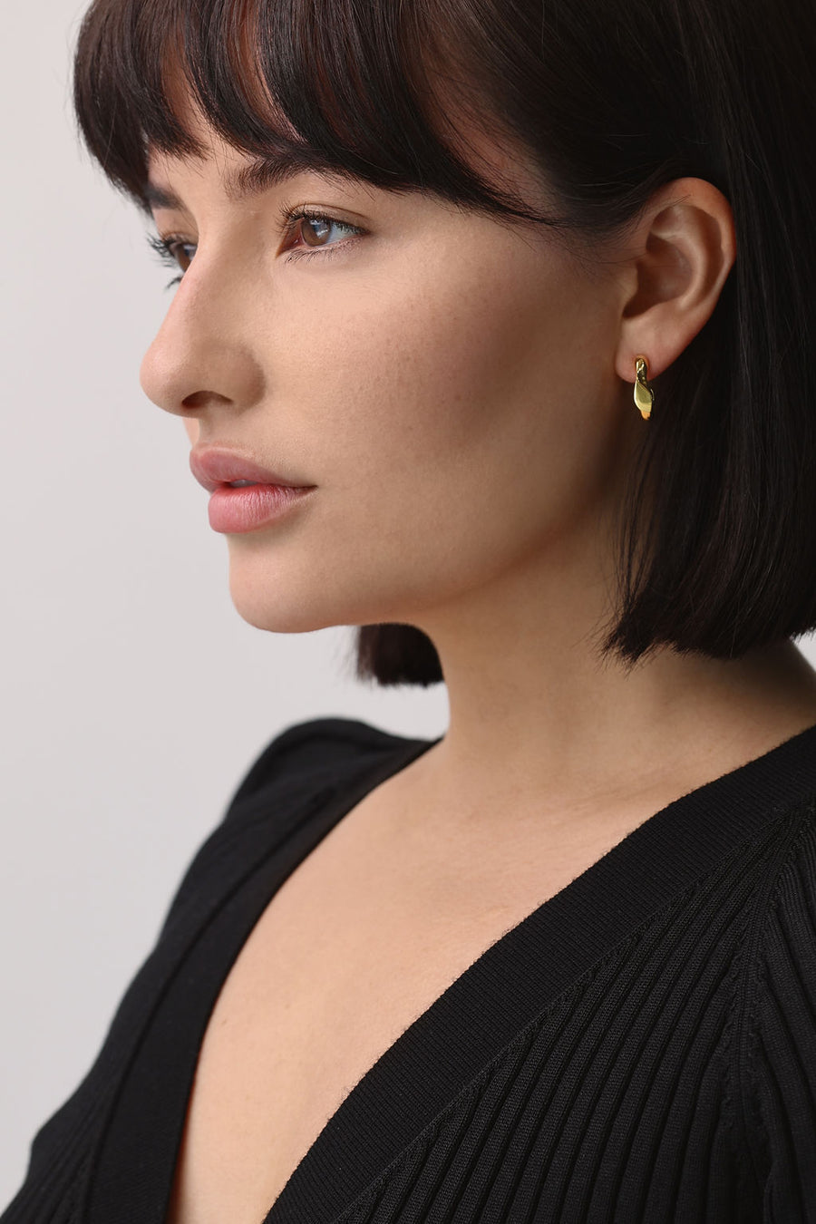 A woman's profile, showing off the small gold irregular hoop she is wearing