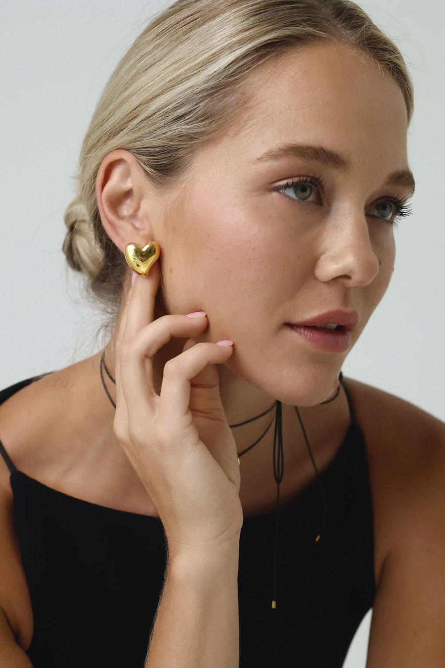 image of woman with blonde hair in a bun, looking off into the side, with her hand behind her ear, showing her gold heartshaped earring